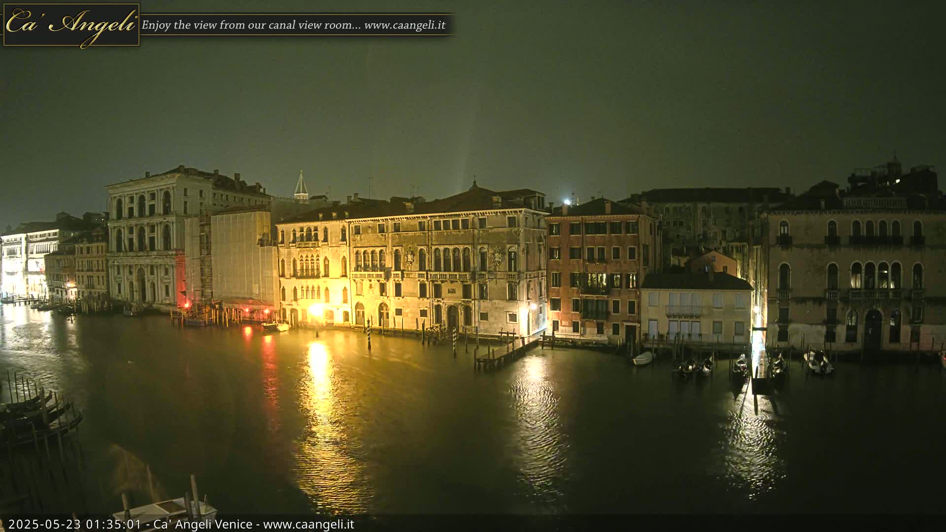 A nighttime view of a canal in Venice, with several buildings lit along its banks under a dark, possibly overcast sky.
