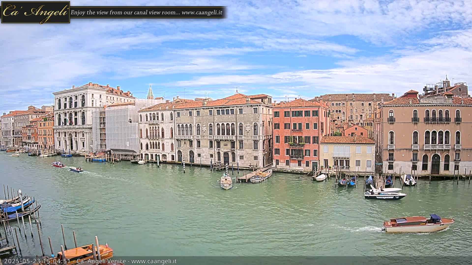 A waterway in Venice, Italy, shows several historic buildings along its banks under a partly sunny sky with some clouds.