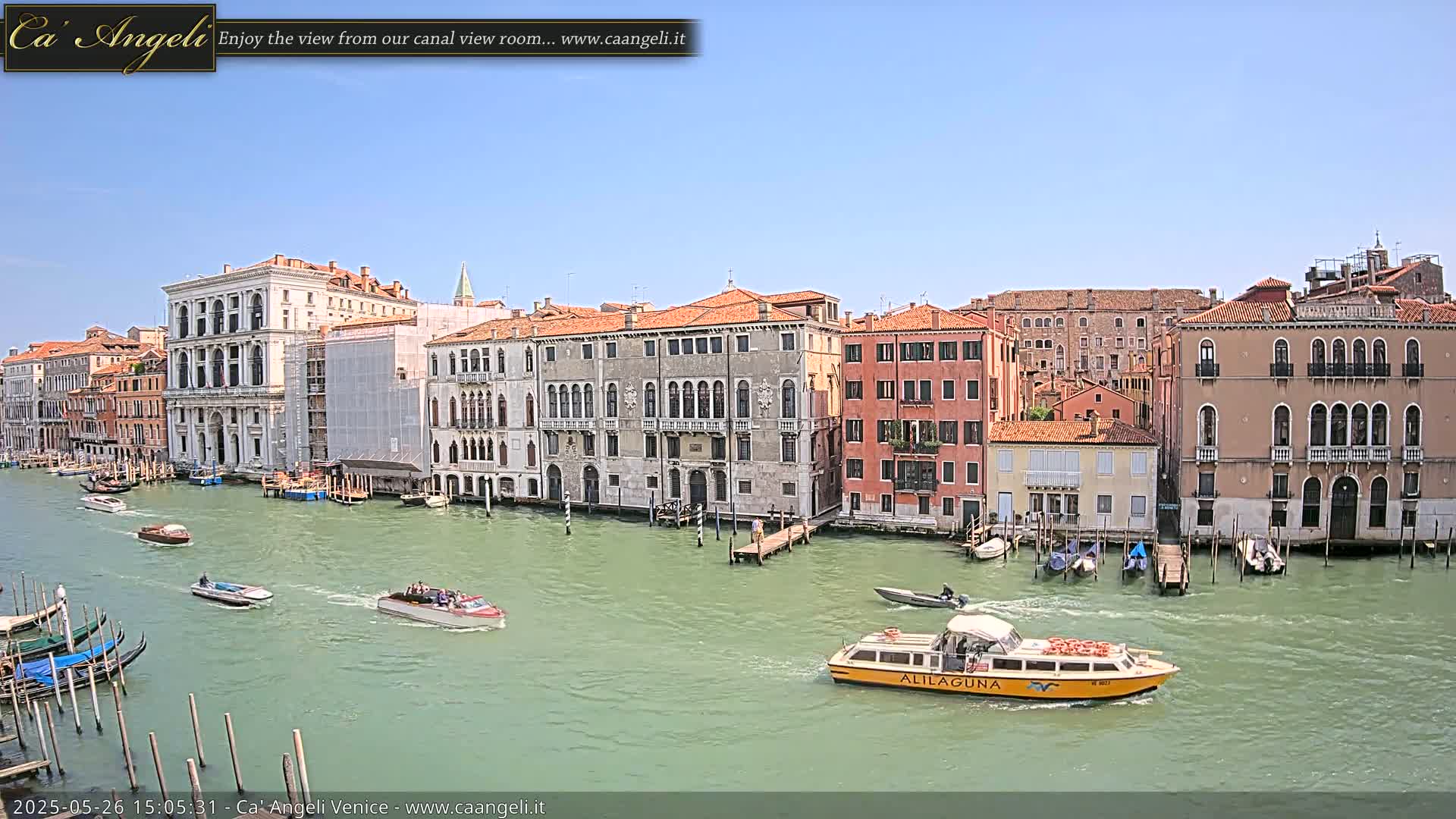 A canal in Venice, under a clear blue sky, is filled with boats and lined with historic buildings.