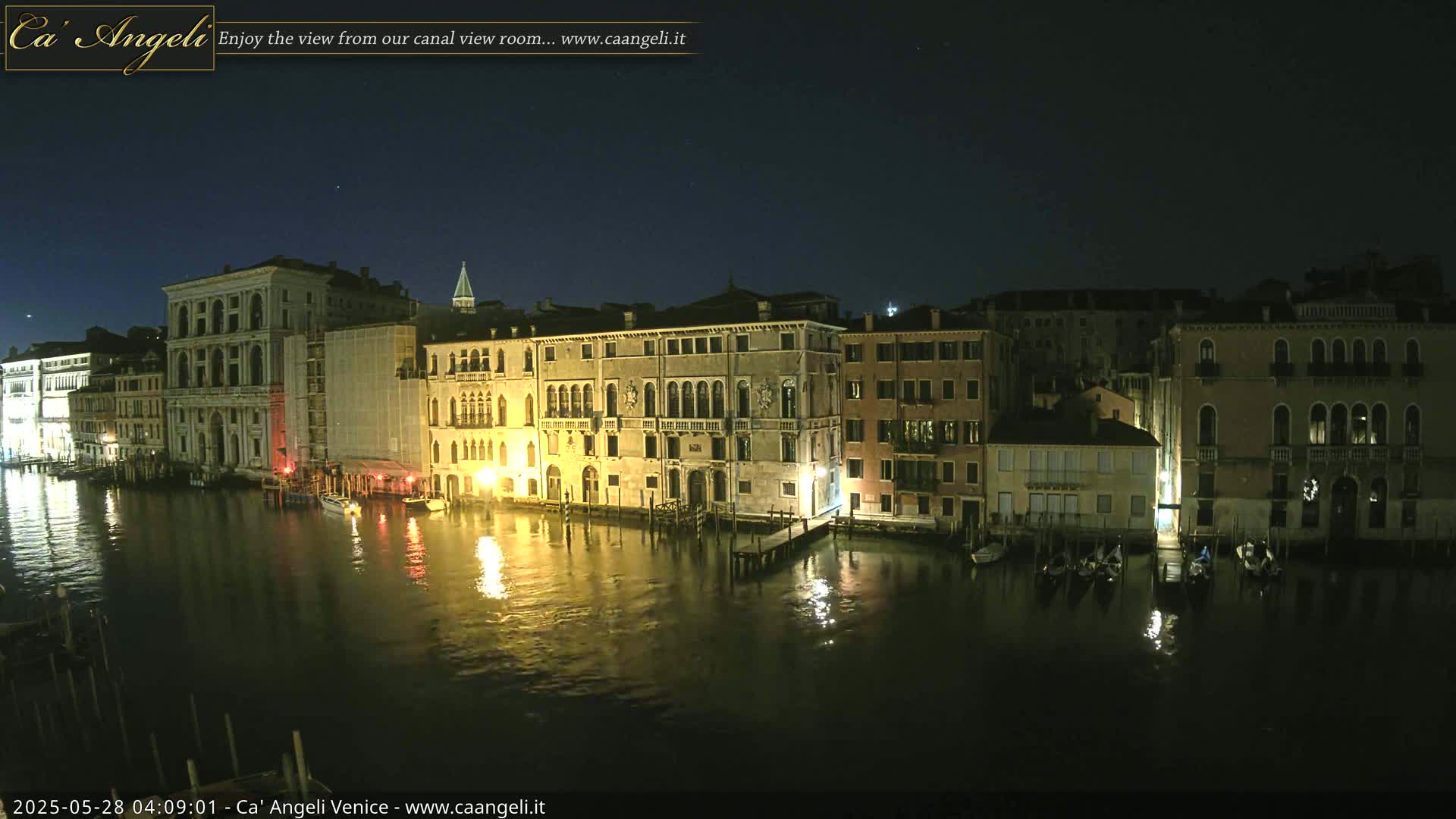 A nighttime view of illuminated buildings along a canal in Venice under a clear, dark sky.