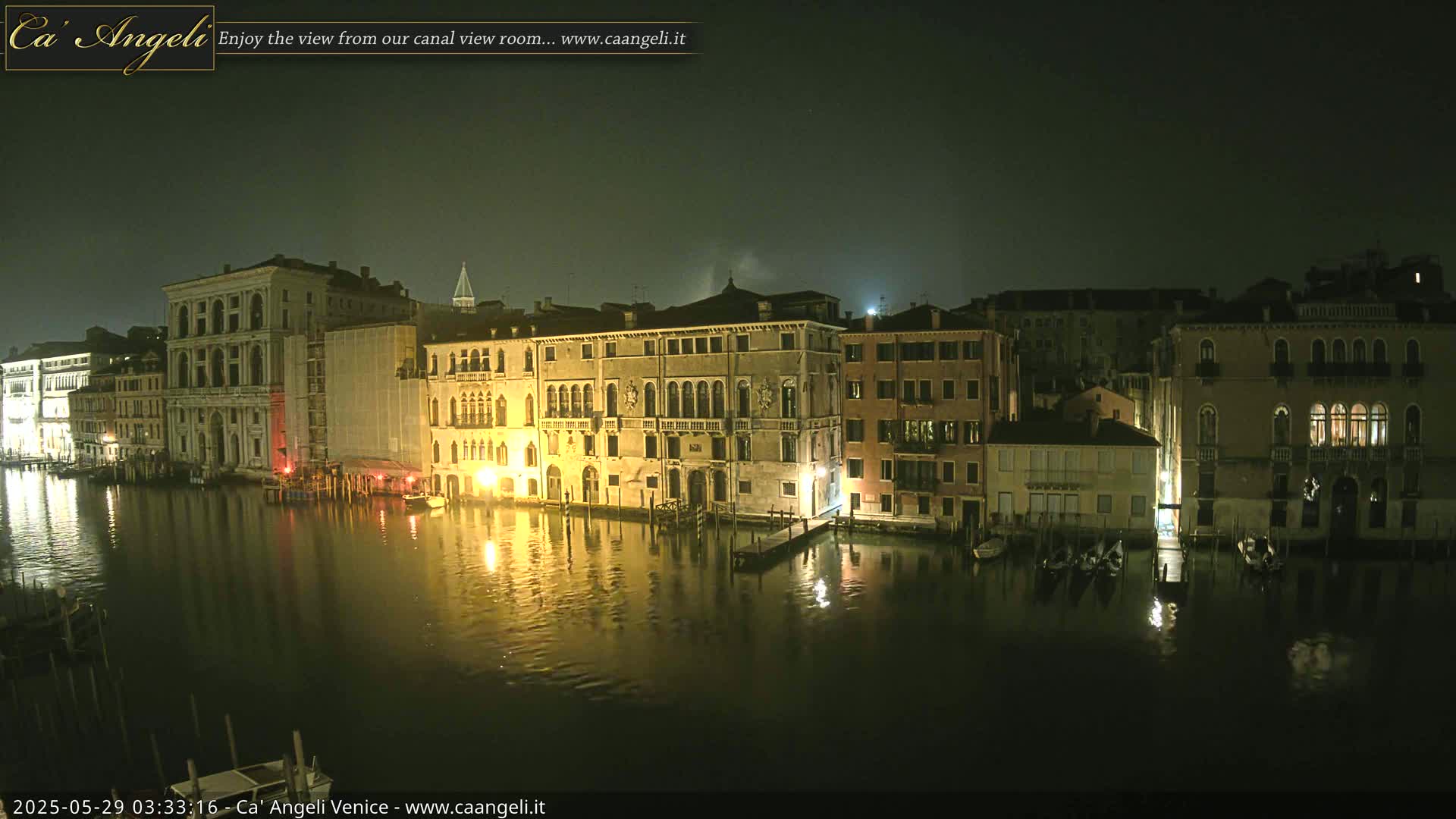 A nighttime view of a canal in Venice, showing several illuminated buildings reflected in the dark water.