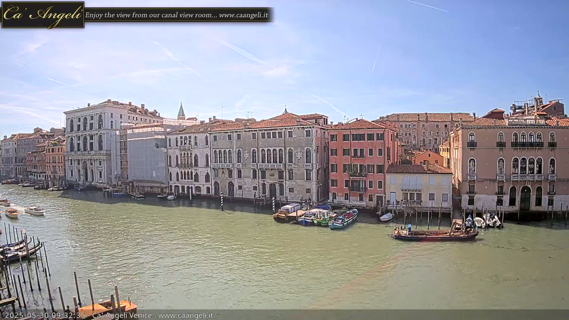 A sunny day in Venice shows a wide canal with several boats moored alongside historic buildings lining the waterway.