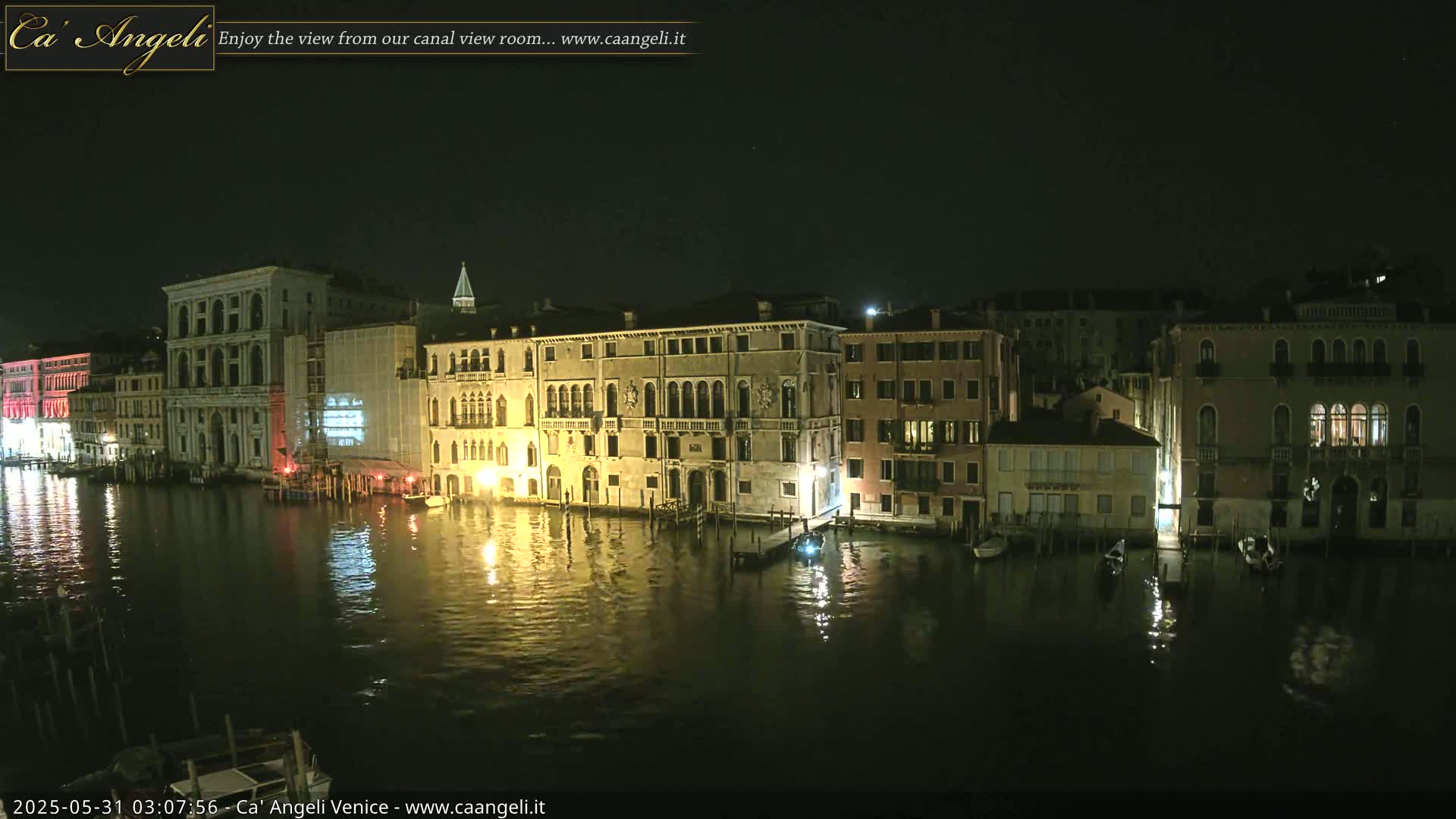 A nighttime view of a calm canal in Venice, lined with illuminated buildings.