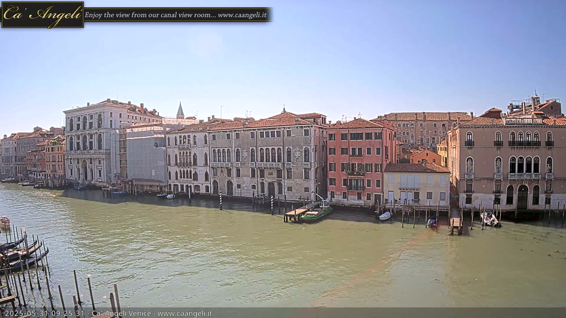 A sunny day reveals a Venetian canal lined with historic buildings, gondolas moored along the edge, and several small boats on the water.