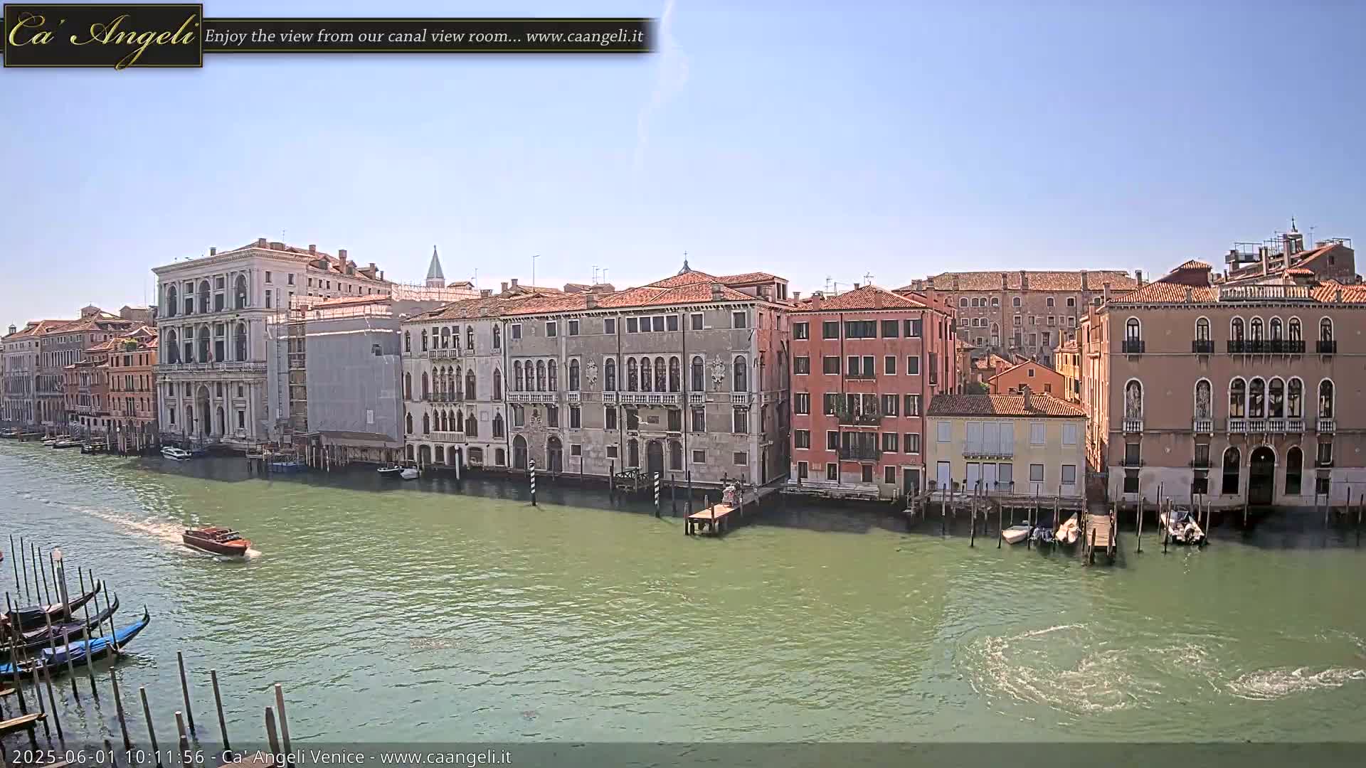 A sunny day in Venice shows a canal with several gondolas and a motorboat, lined by historic buildings along the waterway.