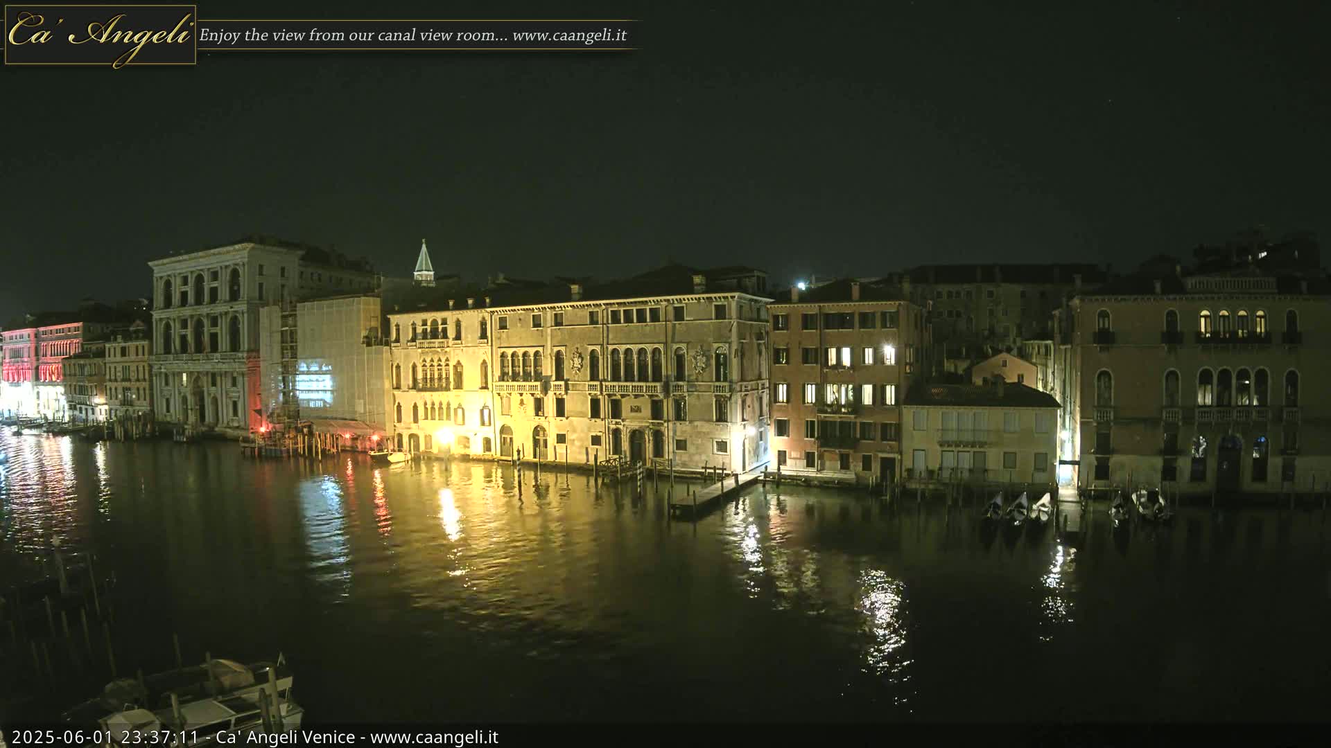 A nighttime view of illuminated buildings lining a calm canal, reflecting the lights on the water.