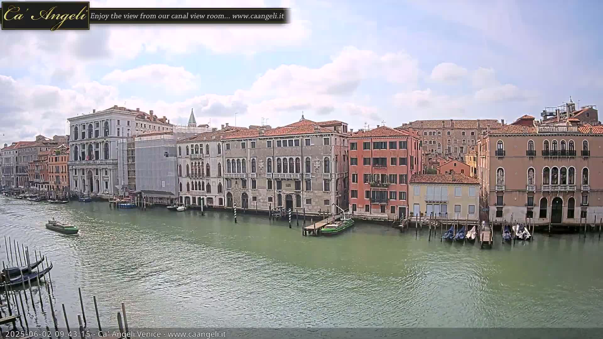 A canal in Venice, under a partly cloudy sky, shows several historic buildings lining its banks, with boats moored along the waterfront.