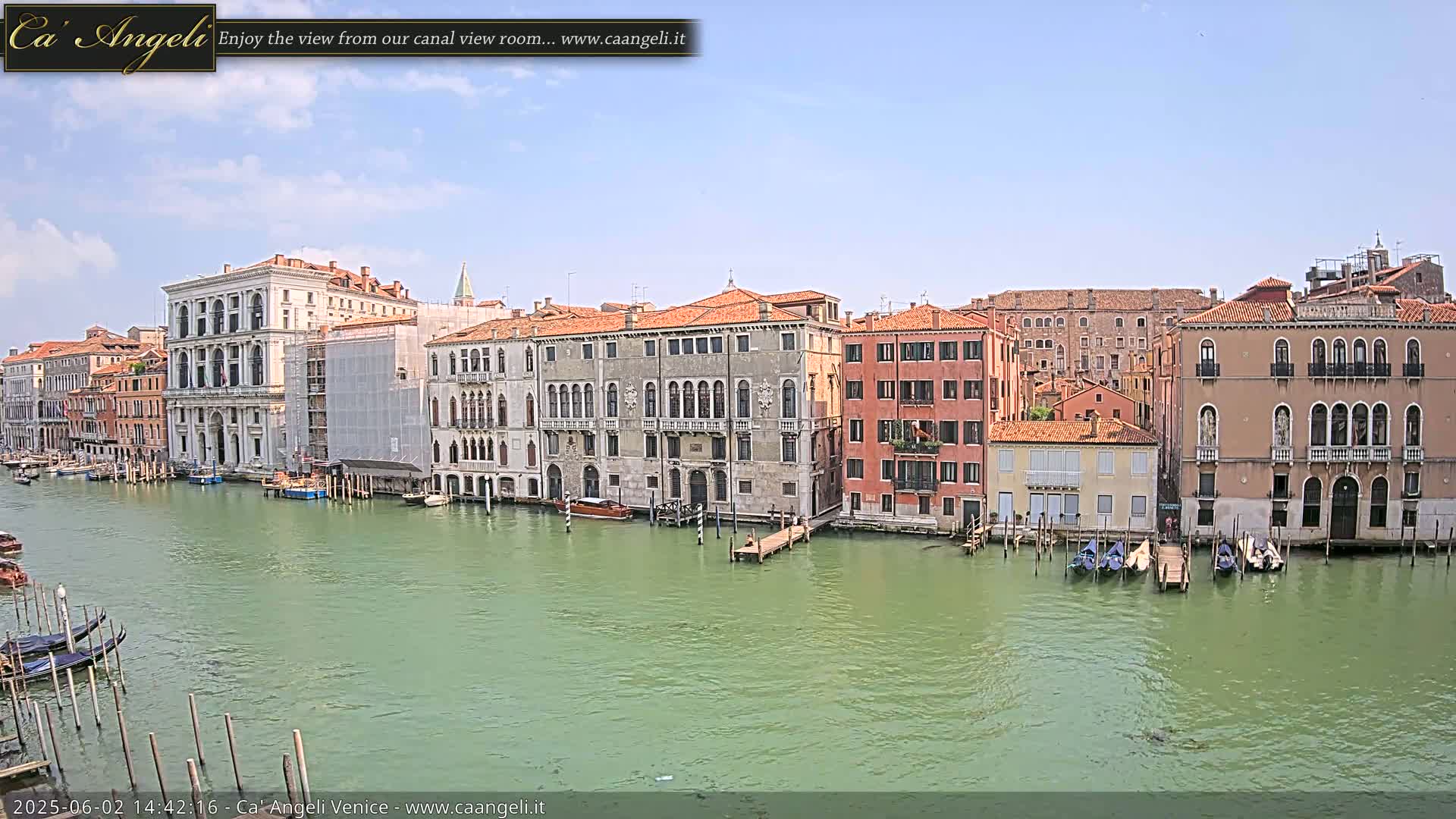 A sunny day in Venice shows several historic buildings lining a canal, with gondolas moored along the waterfront.