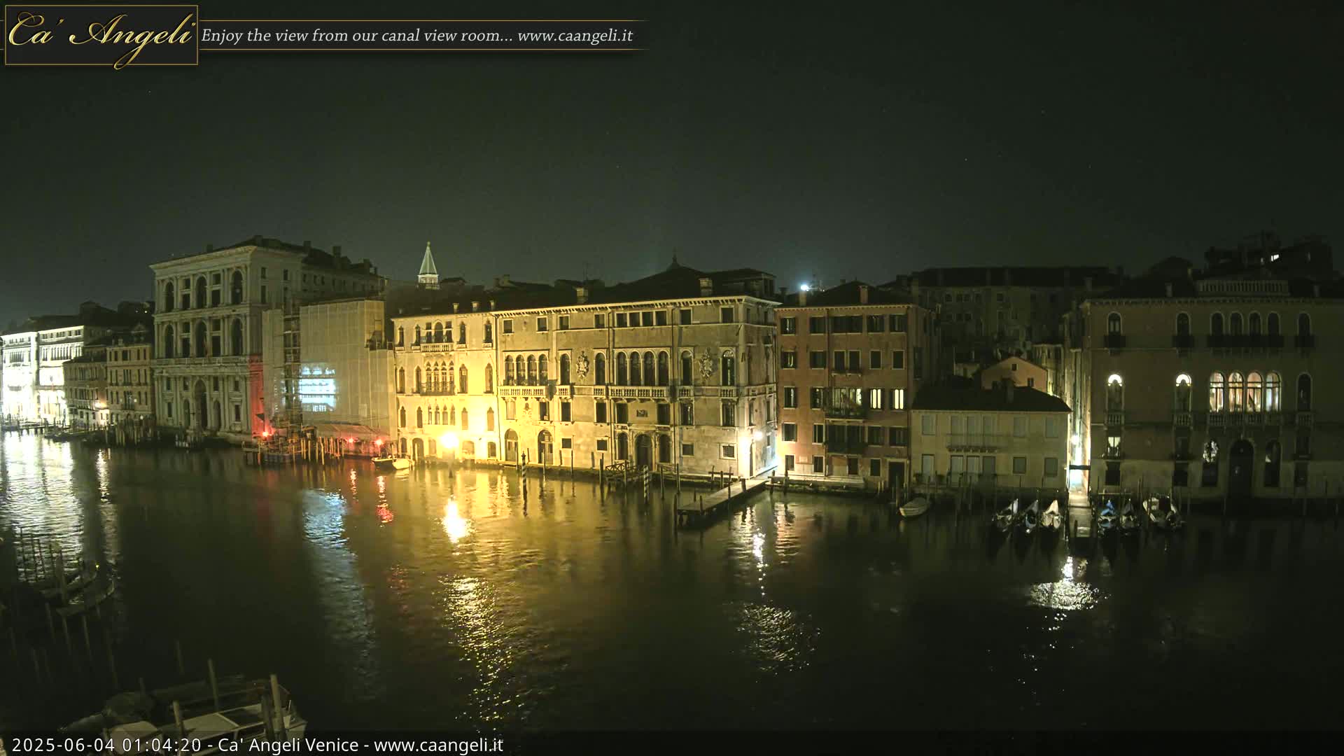 A nighttime view of illuminated buildings lining a canal in Venice, under a dark sky.