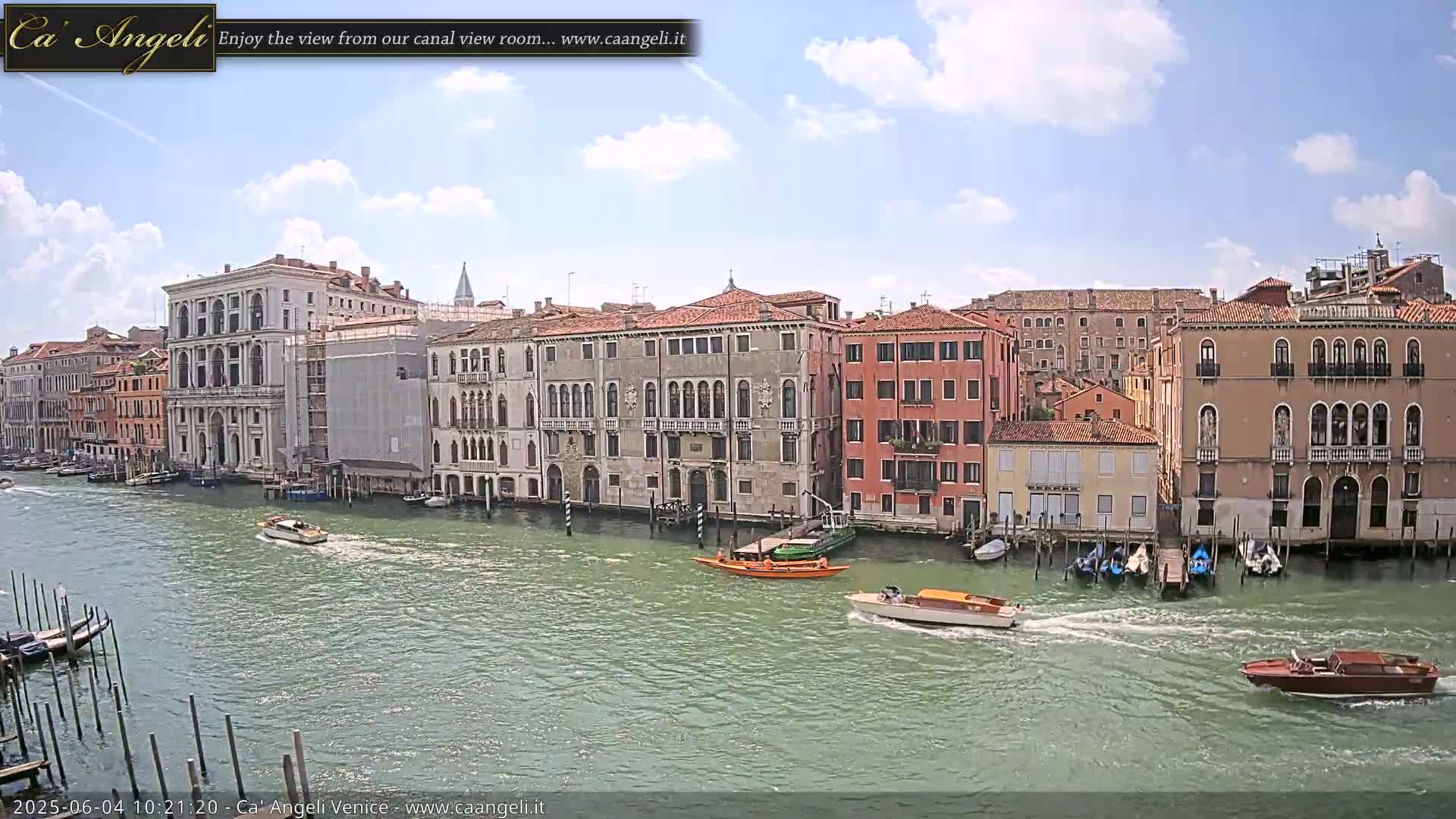 Under a partly cloudy sky, several motorboats navigate a canal lined with historic Venetian buildings.