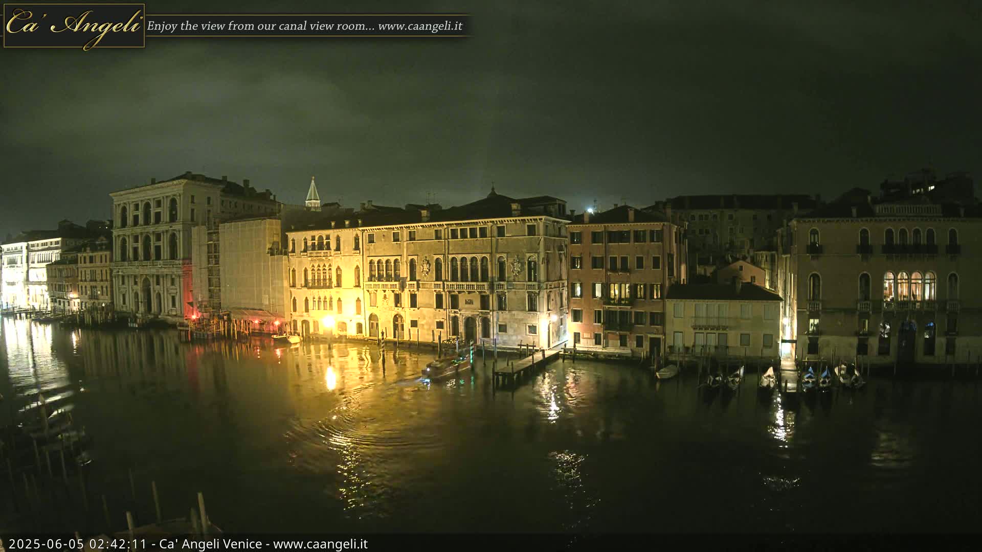 Nighttime view of a canal in Venice, with several illuminated buildings lining the waterway and gondolas moored along the edges.