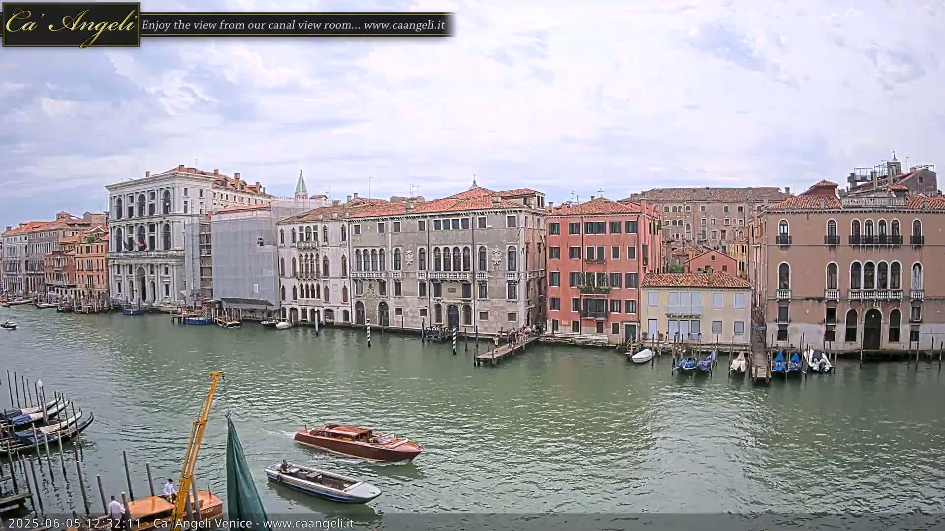 A canal in Venice, under a partly cloudy sky, is lined with numerous historic buildings, and several boats are on the water.