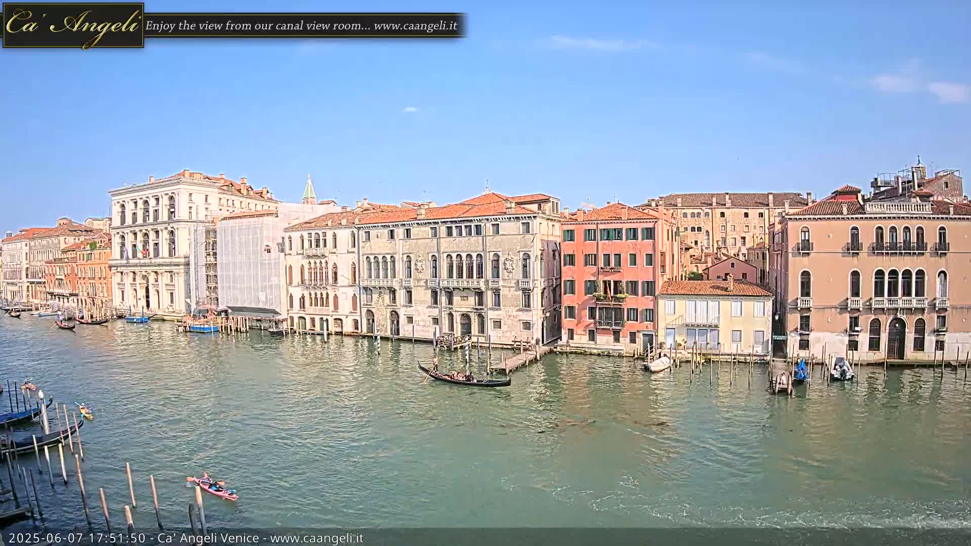 A gondola floats on a calm canal in Venice, Italy, under a clear blue sky, passing colorful buildings and moored boats.