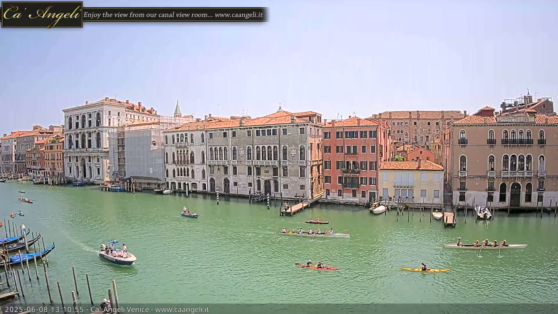 A sunny day in Venice shows several gondolas moored along a canal lined with historic buildings, and several rowing boats and kayaks on the water.