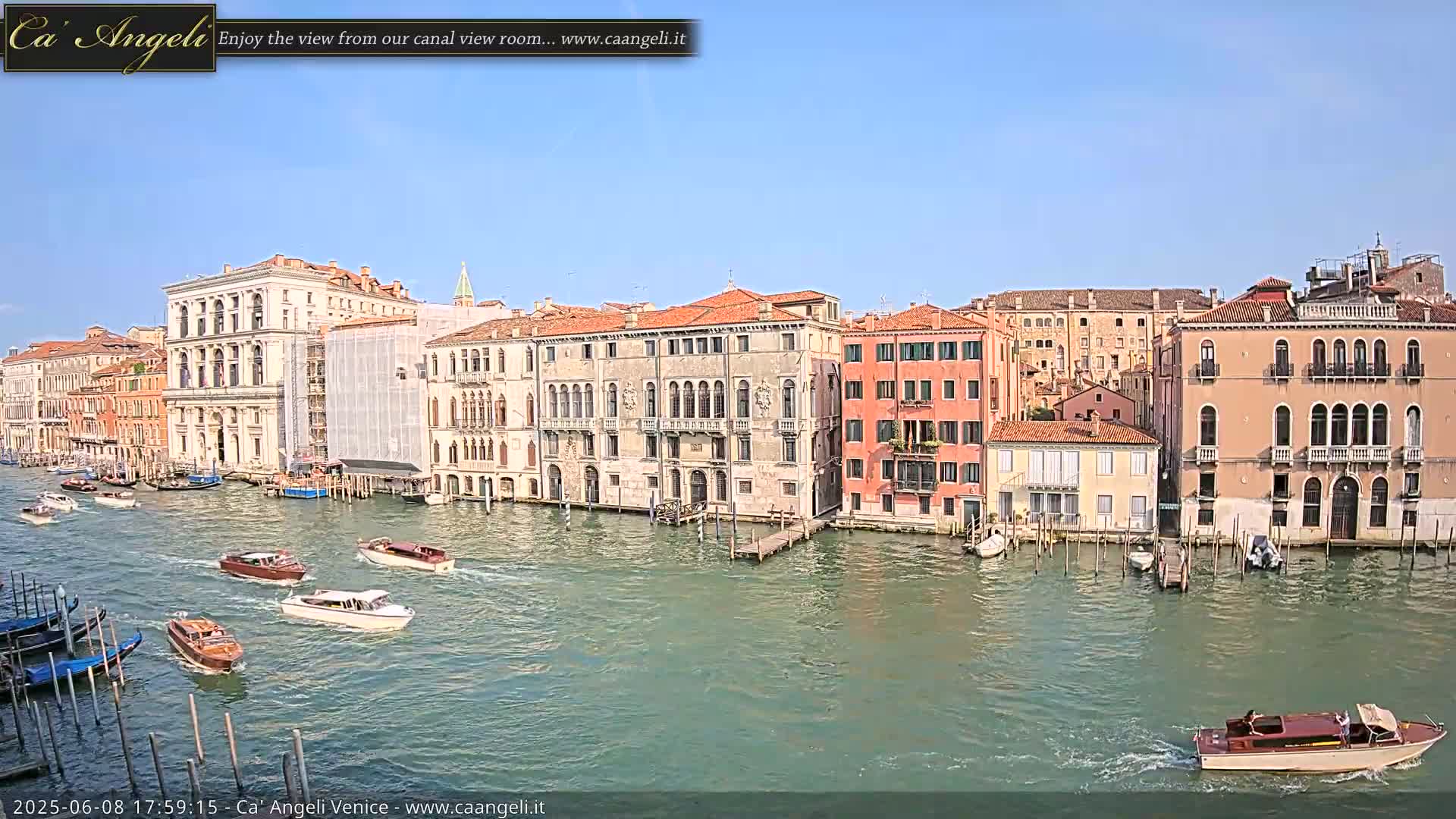 Under a clear blue sky, numerous boats navigate a canal lined with tall, historic Venetian buildings.