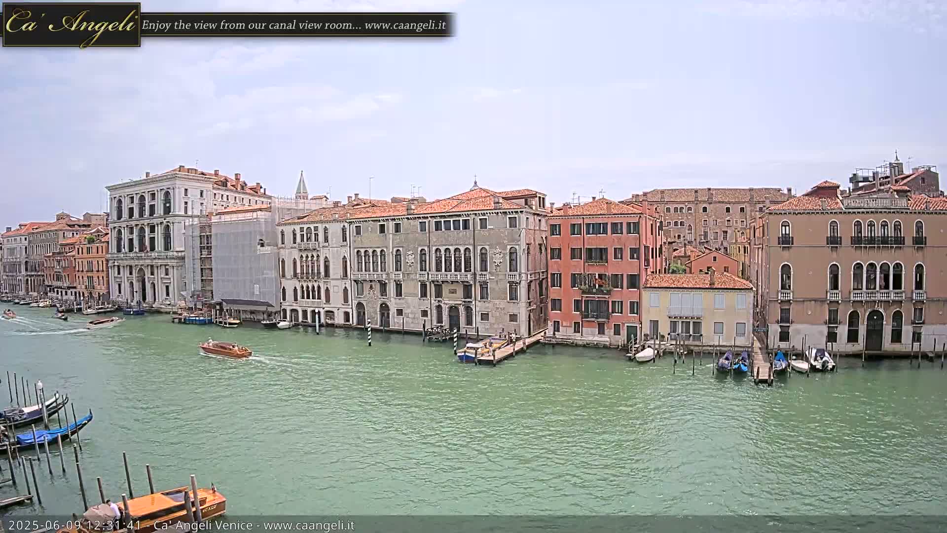 A waterway in Venice, under a mostly cloudy sky, is lined with several multi-story buildings, with boats traveling and moored along the waterfront.