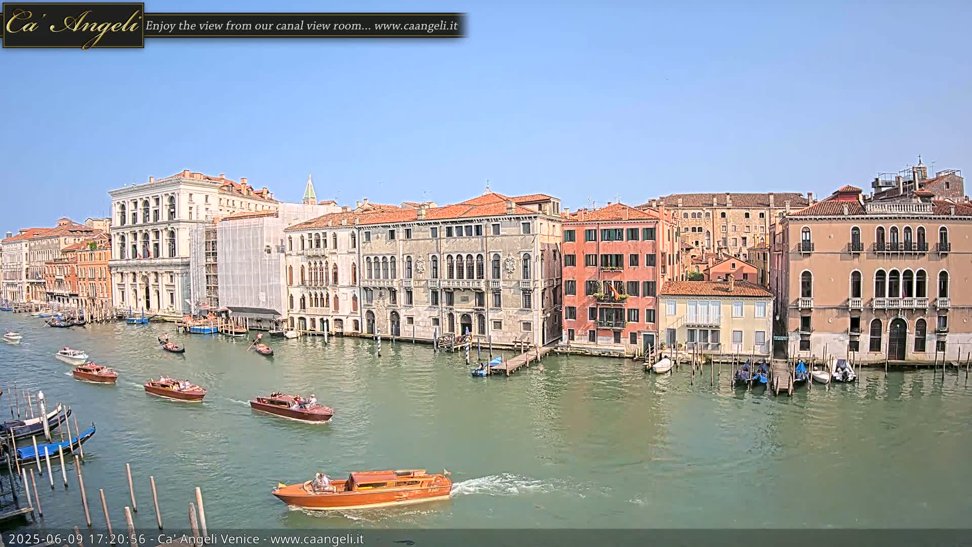 Several boats travel along a canal in Venice, Italy, under a clear blue sky.