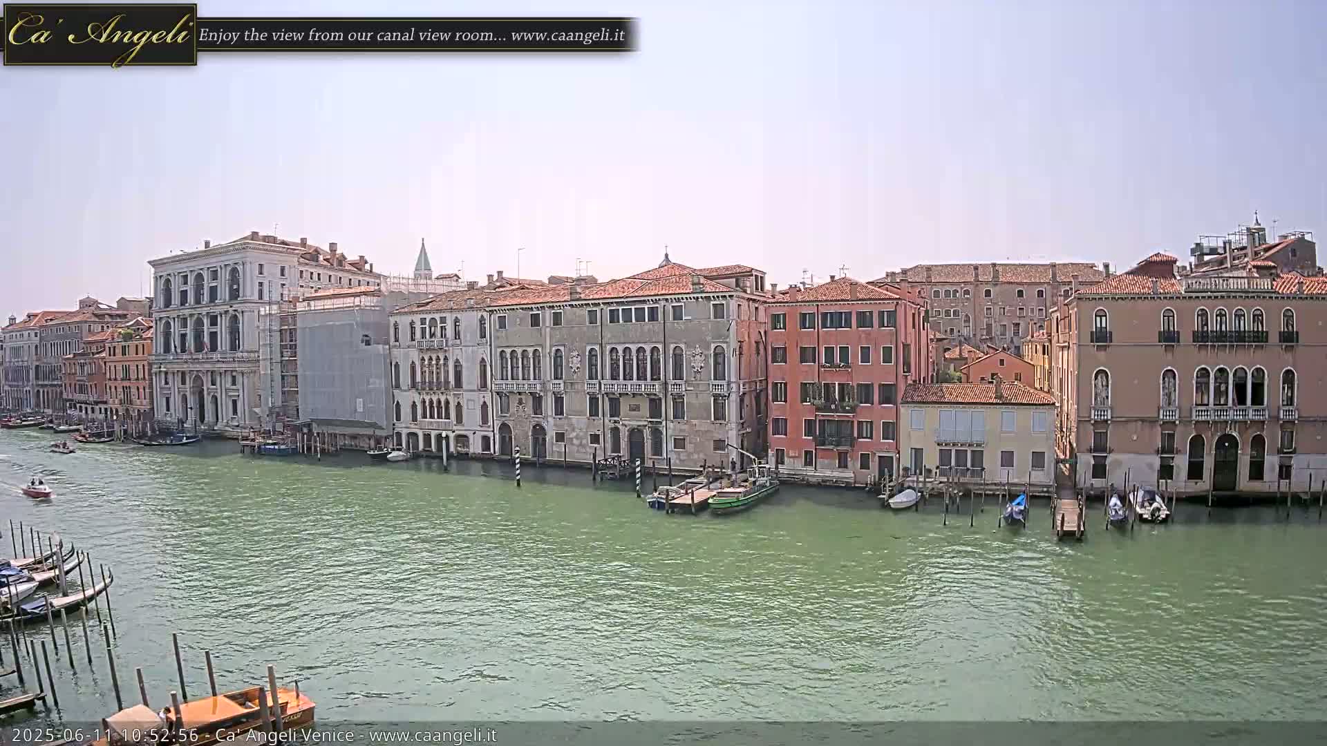 A sunny day shows a view of a canal in Venice, Italy, with numerous buildings lining the waterway and several boats moored along the sides.