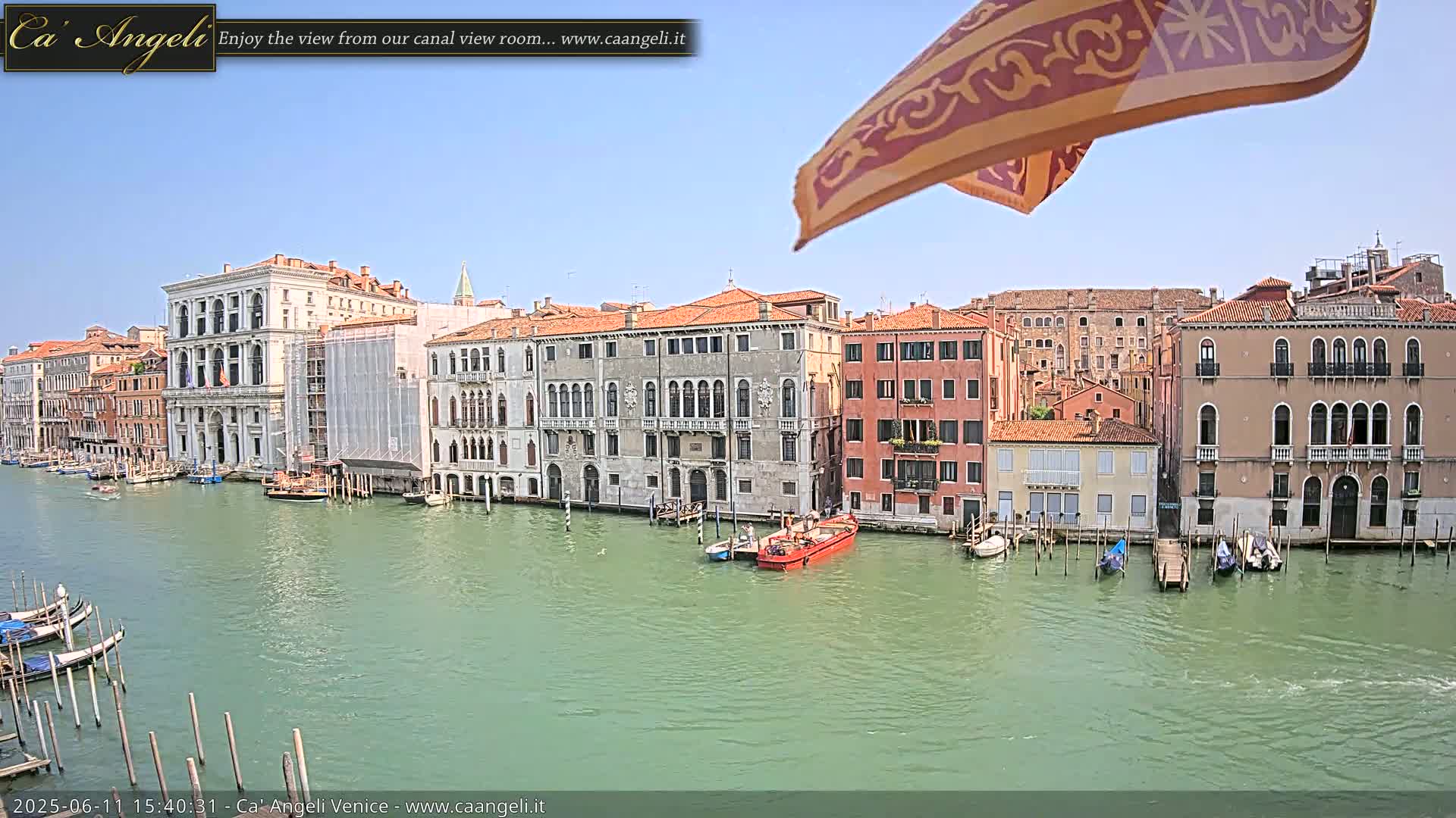 A sunny day in Venice shows a canal lined with historic buildings, gondolas moored along the bank, and a small boat in the waterway.