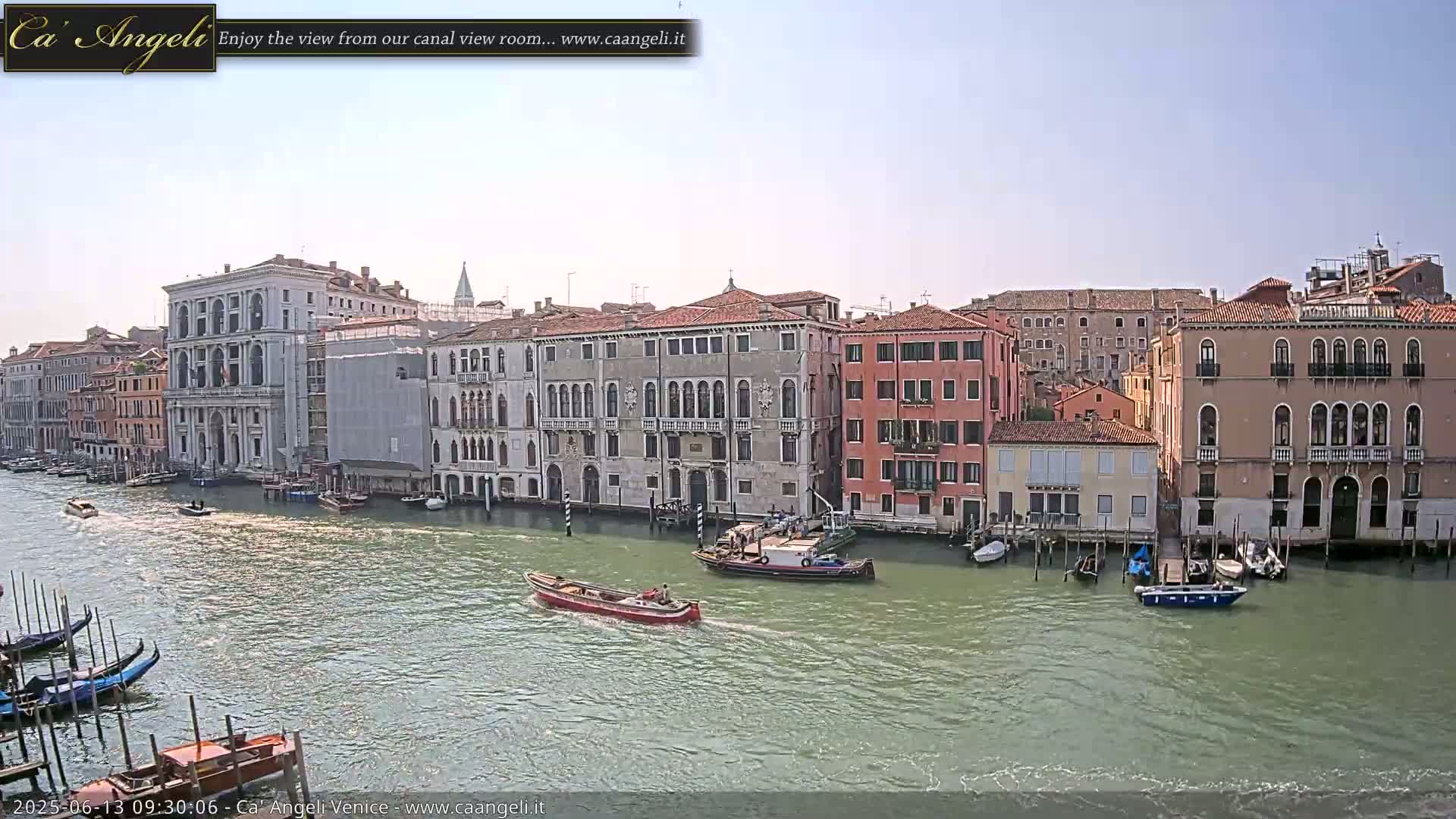 A canal in Venice, under a clear sky, is lined with historic buildings and several boats are visible on the water.