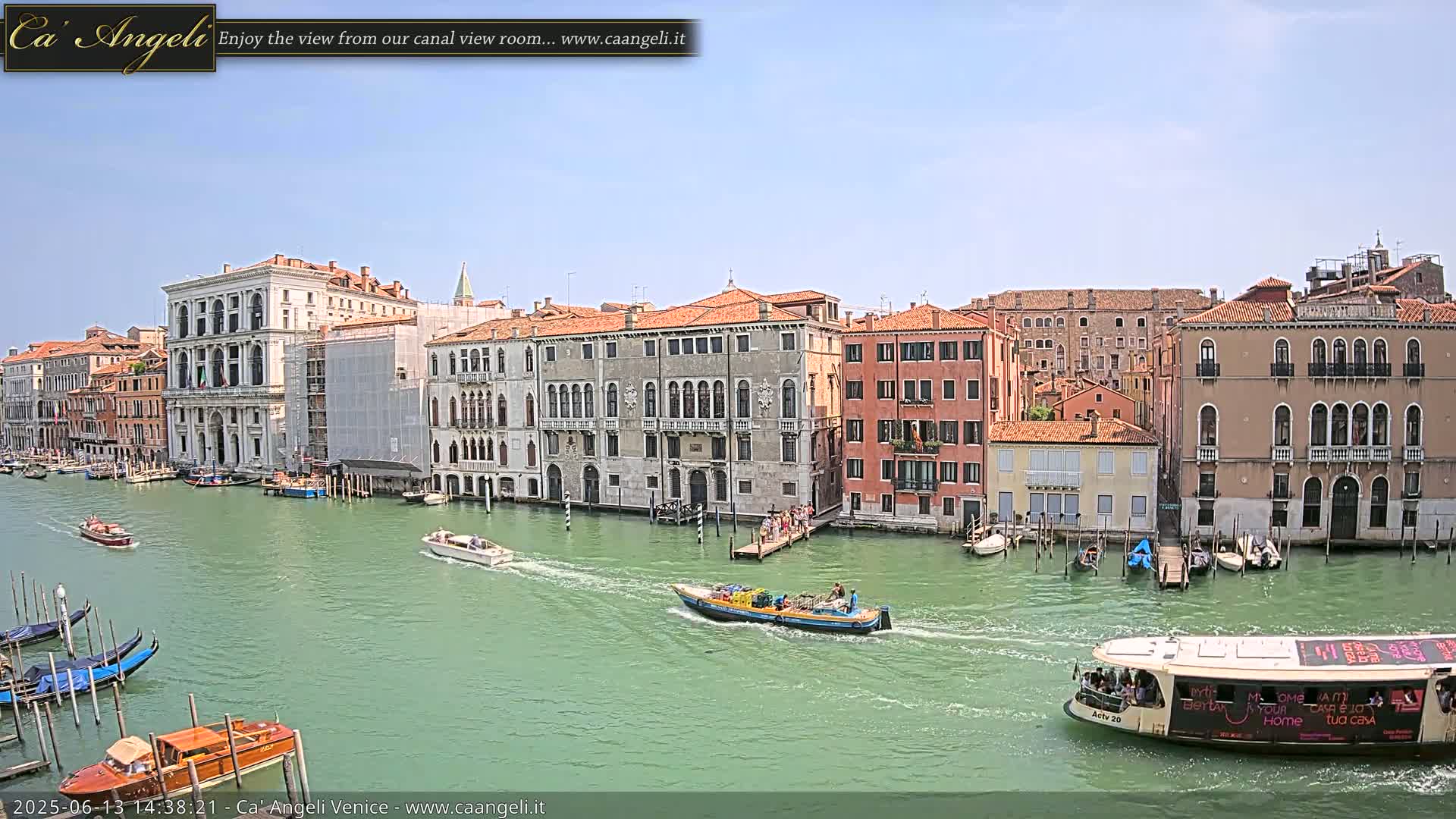 A sunny day in Venice shows a canal with several boats, gondolas, and buildings lining the waterway.