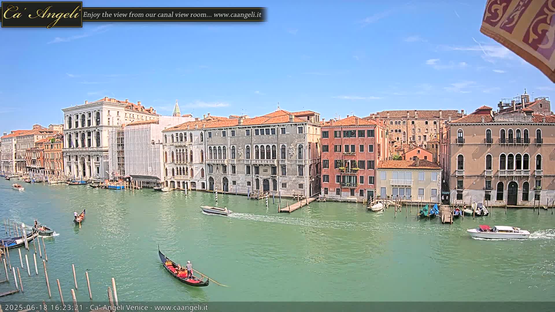 A sunny day in Venice shows several gondolas on a canal lined with historic buildings.
