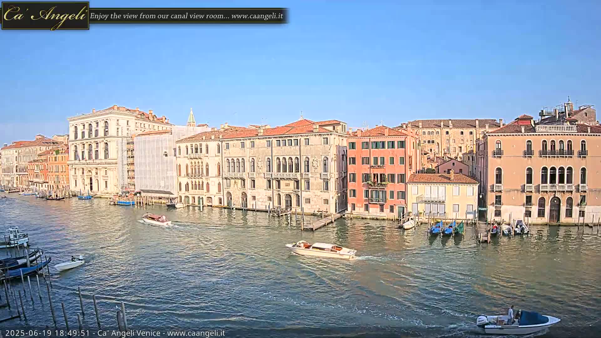 A sunny day in Venice shows several canal-side buildings, boats, and gondolas on a calm waterway.