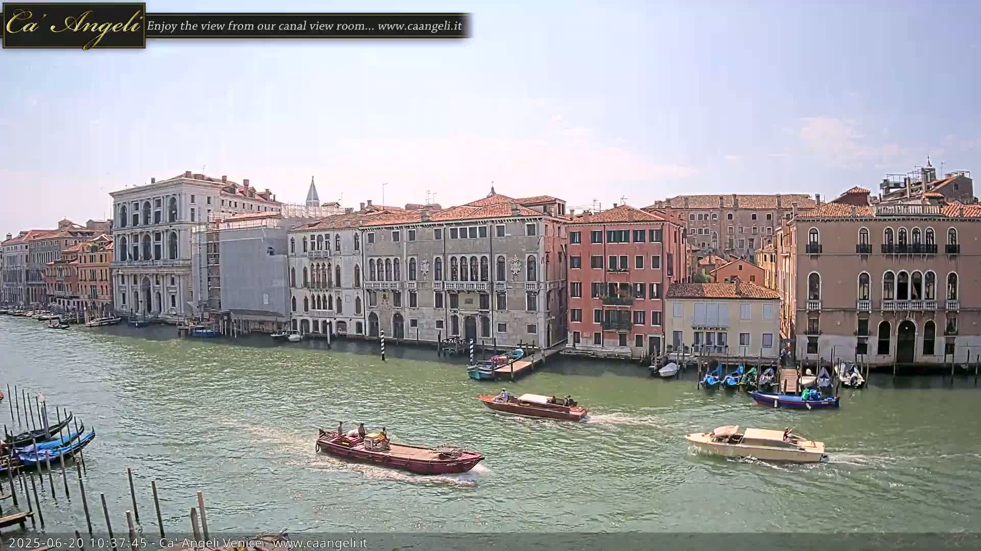 A sunny day in Venice shows several boats moving along a canal lined with historic buildings.