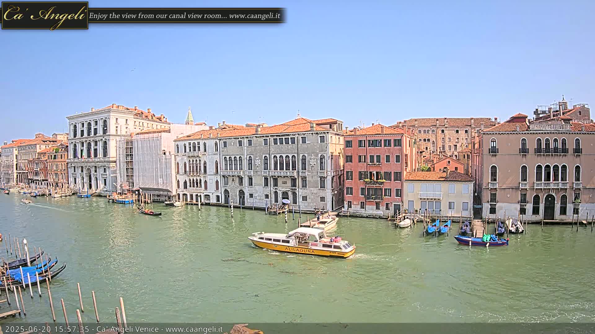 A sunny day in Venice shows a canal with several gondolas and a water taxi passing by numerous buildings along the waterfront.