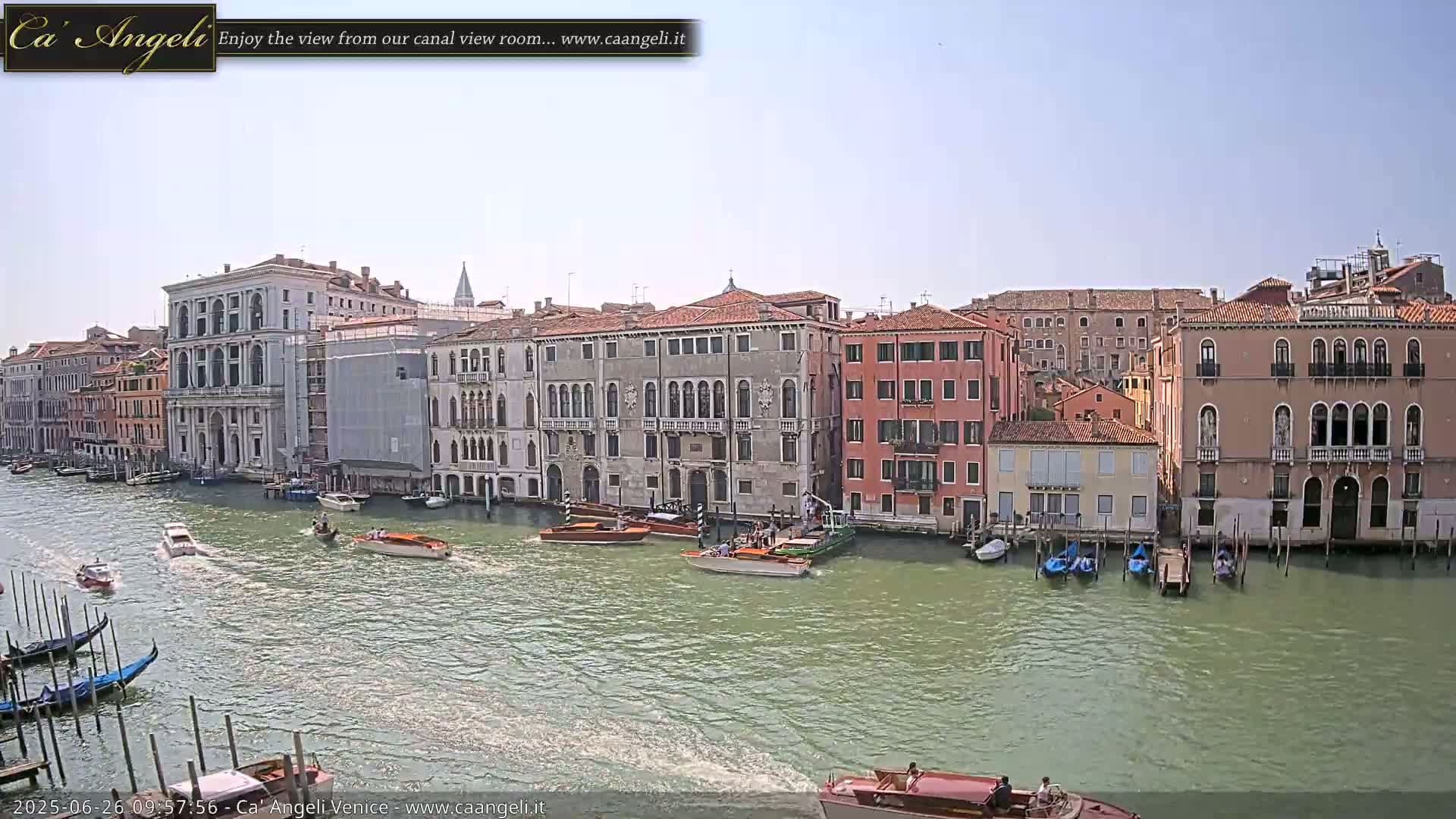 A sunny day in Venice shows several boats traveling on a canal lined with tall, historic buildings.