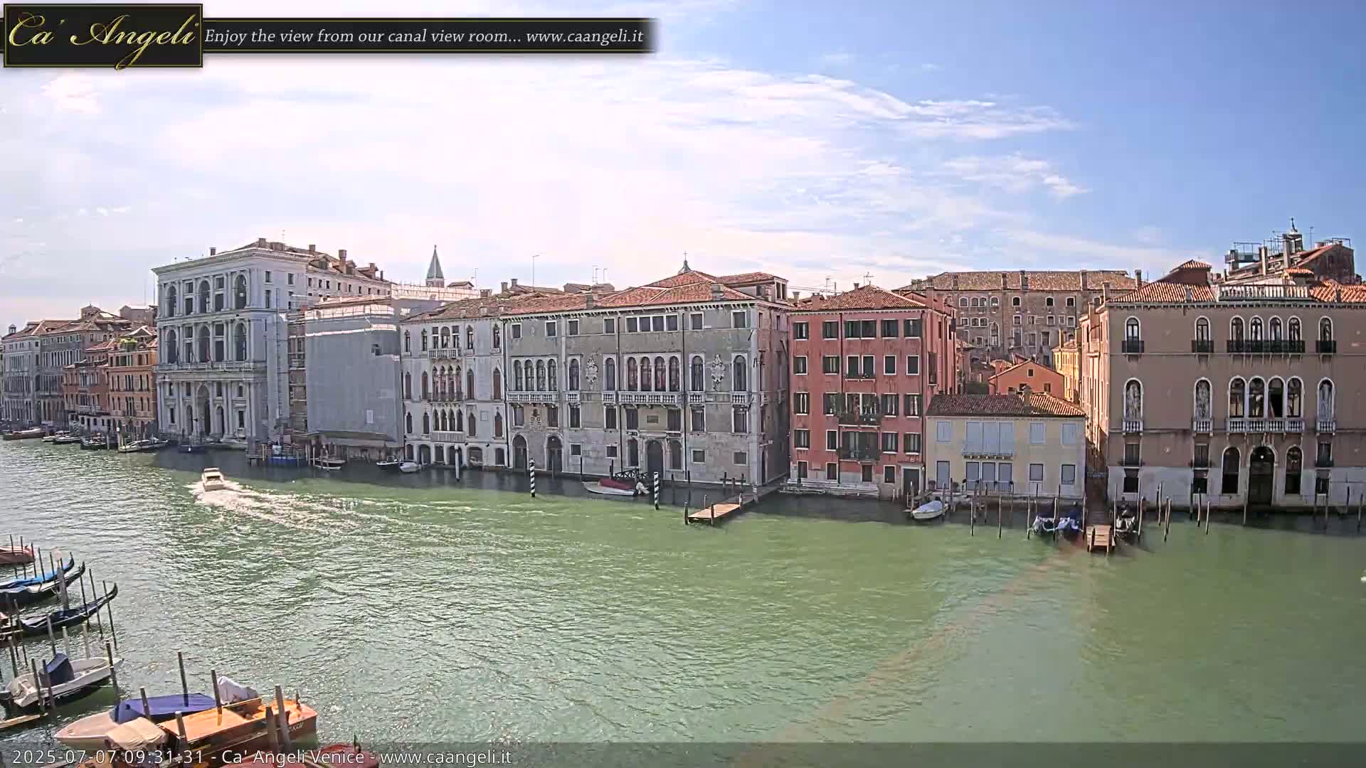 A canal in Venice, under a mostly sunny sky, is lined with historic buildings, and a small motorboat is visible on the water.