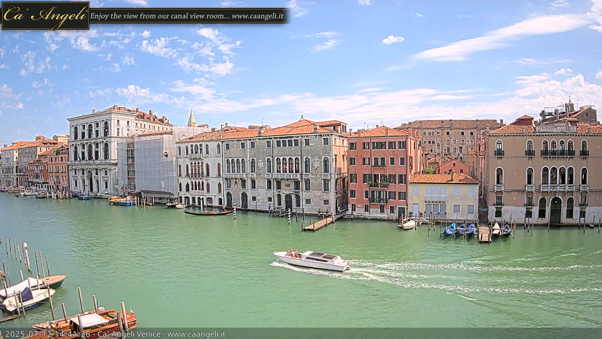 A canal in Venice, under an overcast sky, is lined with several multi-story buildings, with boats moored along the edges and a few others traveling the waterway.
