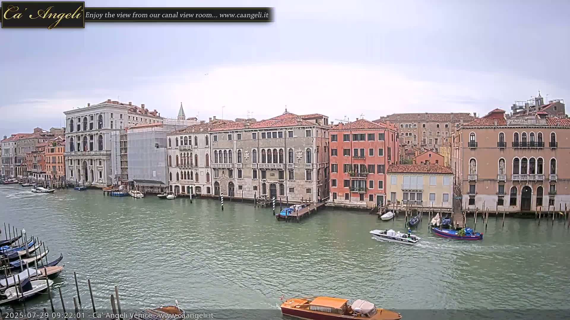A canal in Venice, under an overcast sky, is lined with historic buildings, with several boats and gondolas on the water.