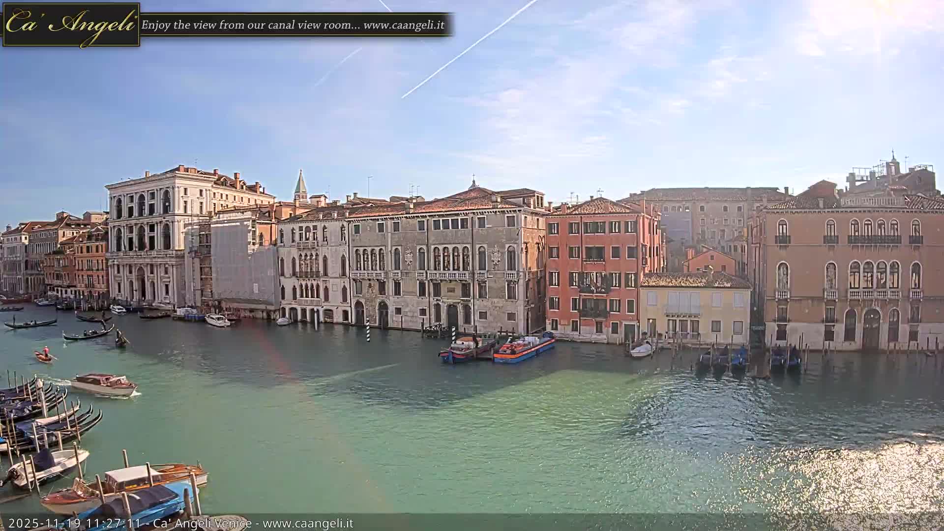 A canal in Venice, under an overcast sky, is lined with historic buildings, with several boats and gondolas on the water.