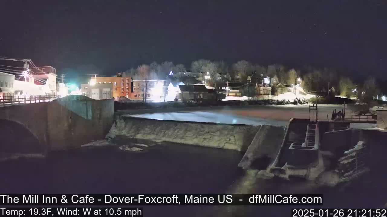 A nighttime view of a town's river dam and buildings under a clear, starry sky.