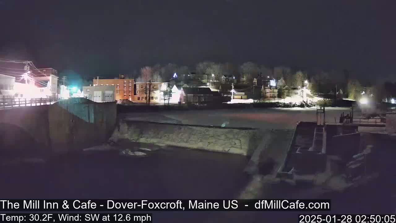 A nighttime view of a snow-covered town beside a river, with a southwest wind at 12.6 mph and a temperature of 30.2°F.