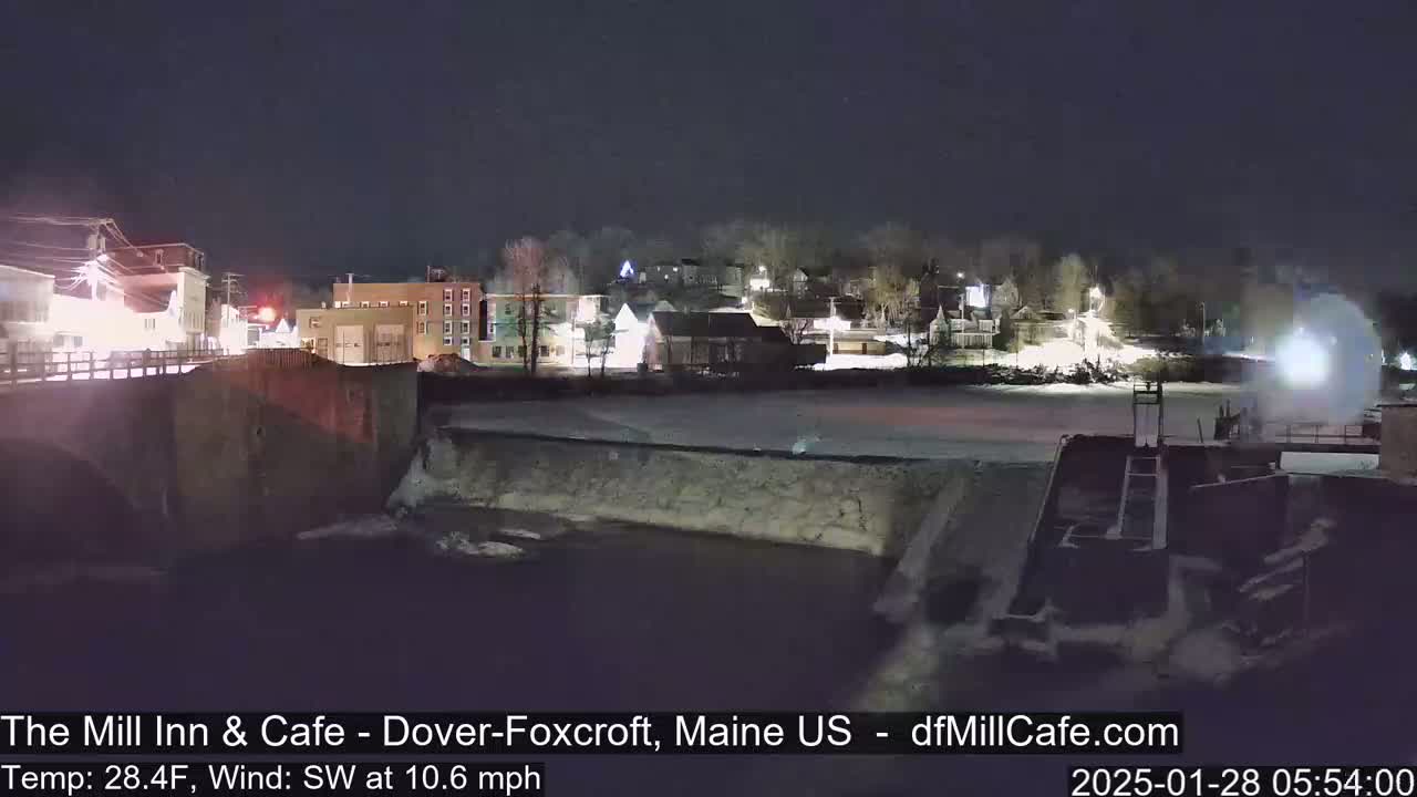 A nighttime view of a town across a river, partially frozen, with a dam and a southwest wind blowing at 10.6 mph and a temperature of 28.4°F.