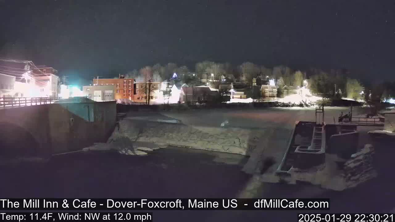 A nighttime view of a snow-covered town beside a partially frozen river under a clear, starry sky.