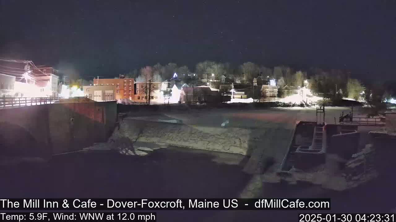 A nighttime view of a snow-covered town beside a frozen river under a clear, starry sky.