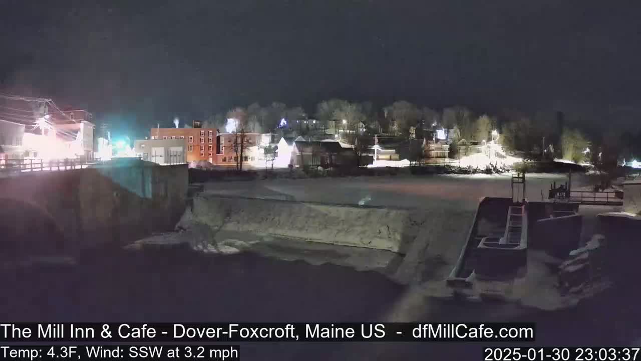 A nighttime view of a snow-covered town near a river, under a dark sky.