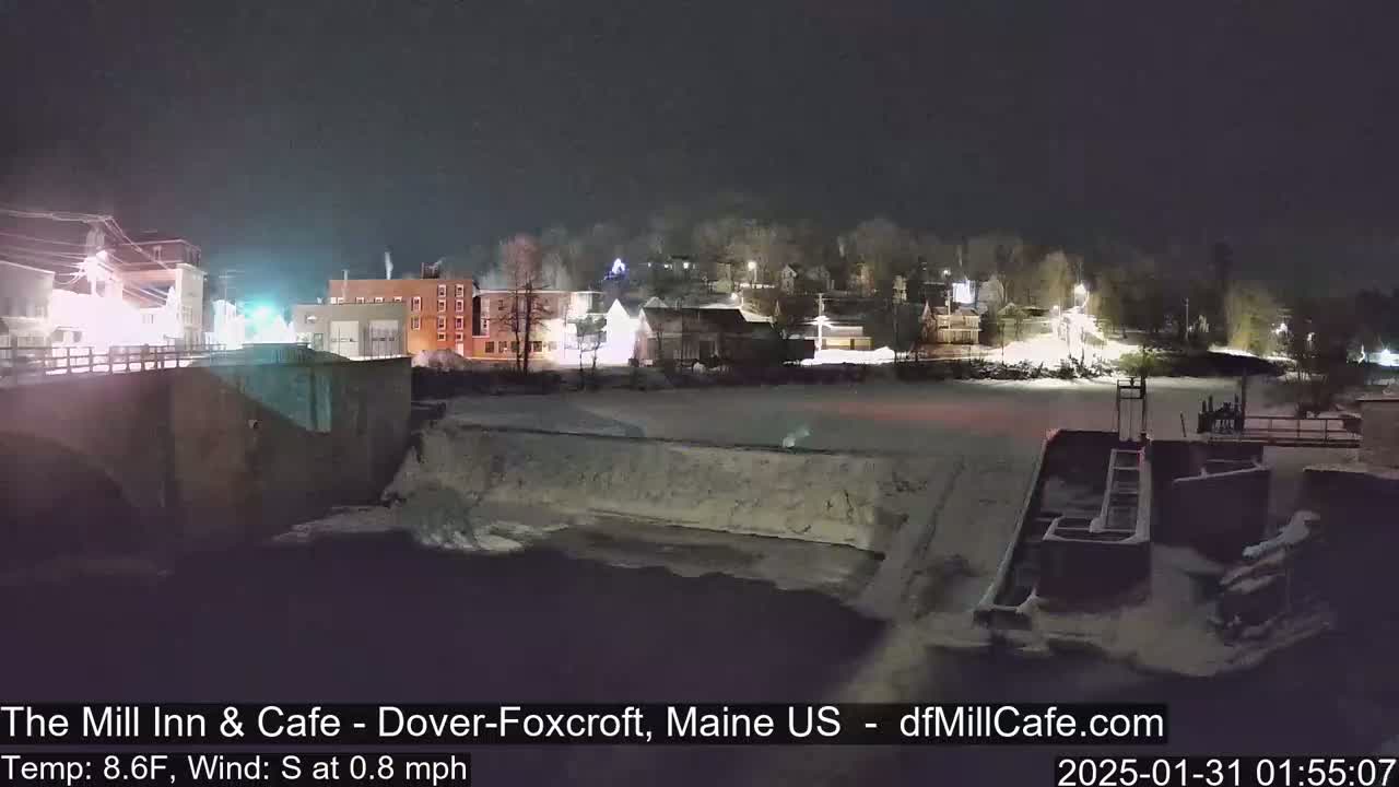 A nighttime view of a snow-covered town beside a river, with a low temperature and a slight south wind.