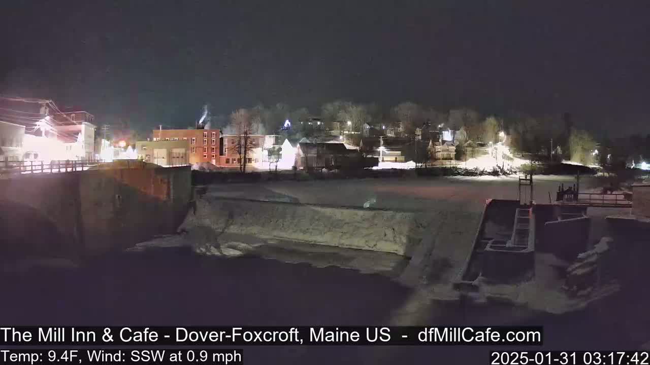 A nighttime view of a snow-covered town beside a frozen waterway under a clear, dark sky.