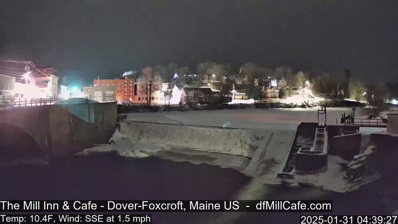 A nighttime view of a snow-covered town beside a partially frozen river, under a dark sky.
