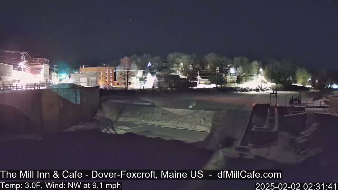 A nighttime view of a snow-covered town beside a partially frozen river, under a clear, starry sky.