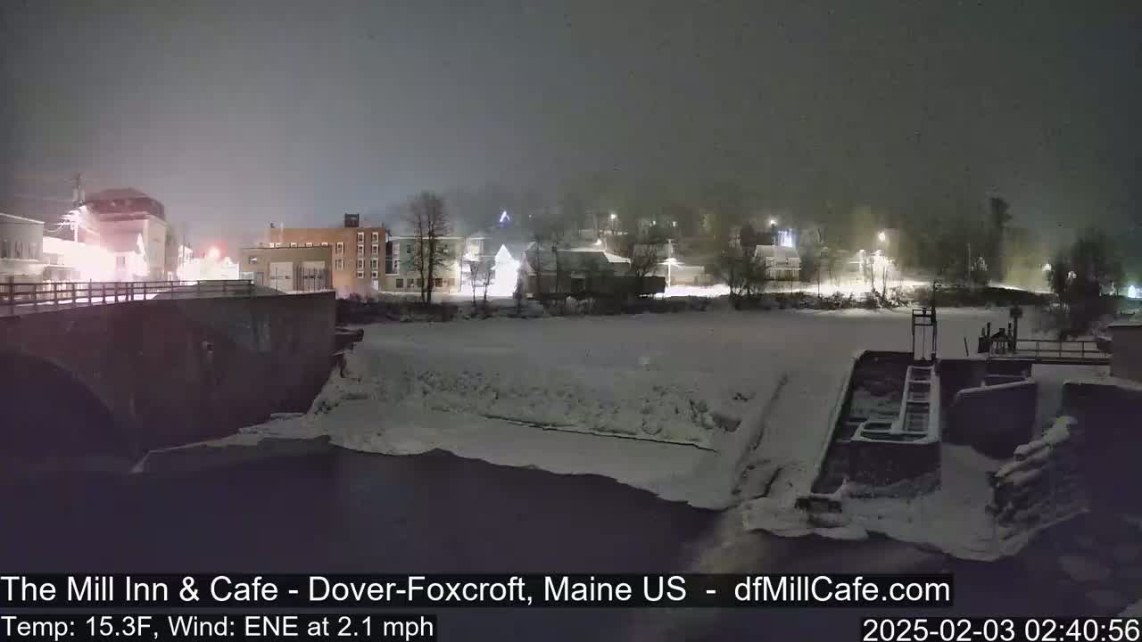 A snow-covered town at night, viewed from a bridge over a partially frozen river.