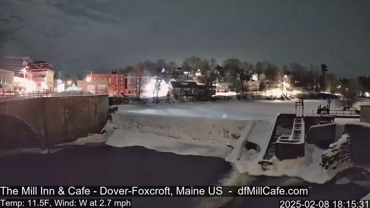 A nighttime view of a snow-covered town and river with a dam, under a dark sky.