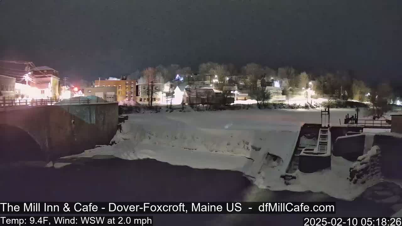 A snow-covered river flows past a town at night, under a dark sky.