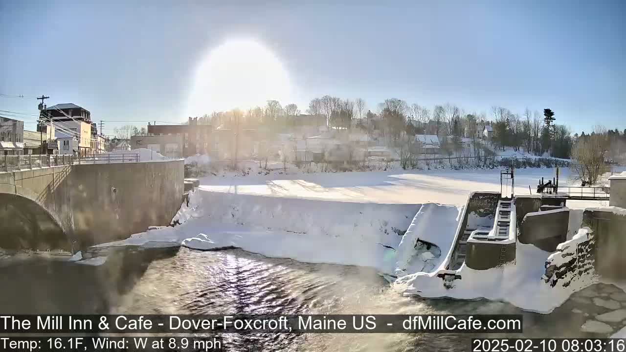 A snow-covered dam and river are seen on a sunny, cold winter day.