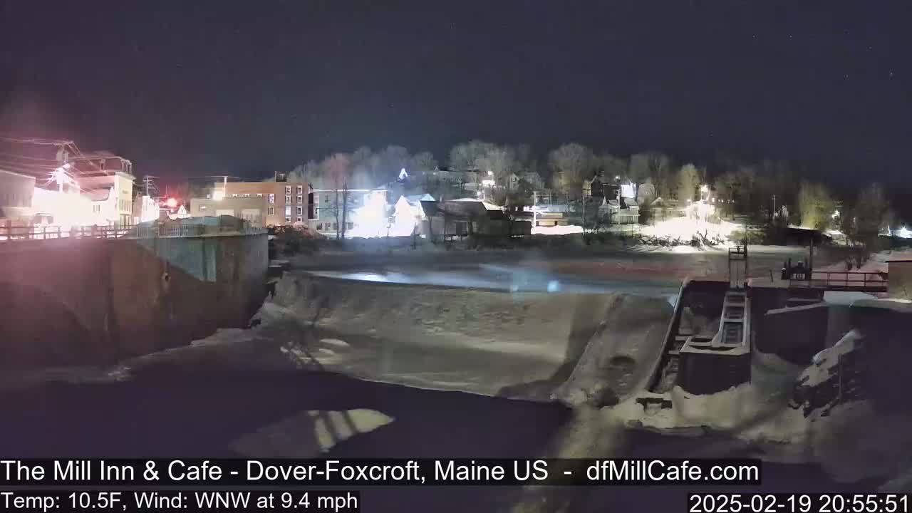 A nighttime view of a snow-covered town beside a partially frozen river under a clear, dark sky.