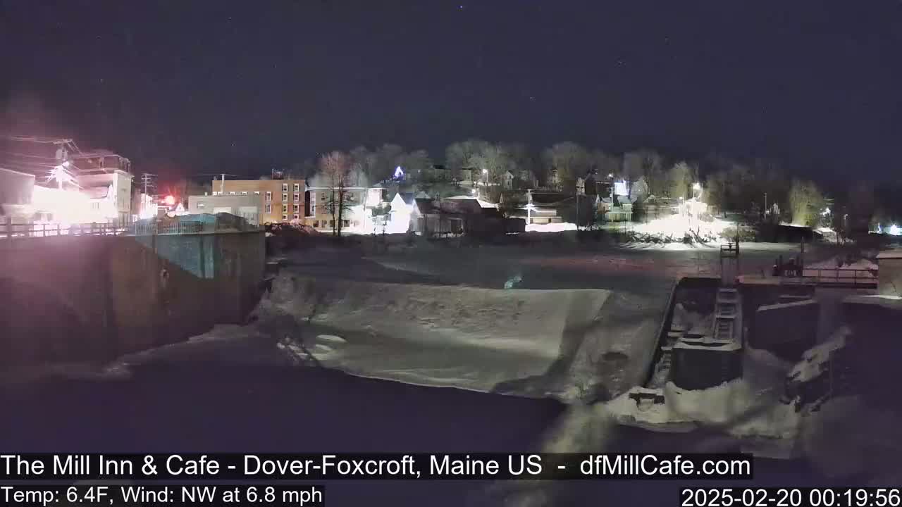 A nighttime view of a snow-covered town beside a frozen river, under a clear, starry sky.